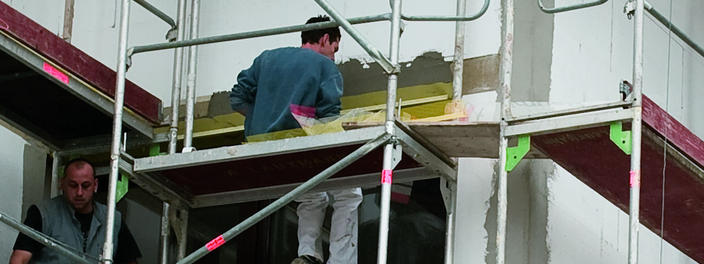 Gebäudesanierung, Handwerker stehen auf einem Gerüst und arbeiten an Gebäudefassade