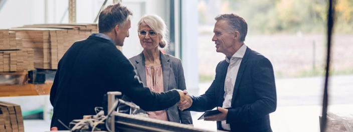 Shake-hands zwischen Bankberater und Mann in Produktionshalle, neben Geschäftsführerin