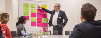 Mann zeigt vor Zuhörern auf Post-its an Flip-Chart