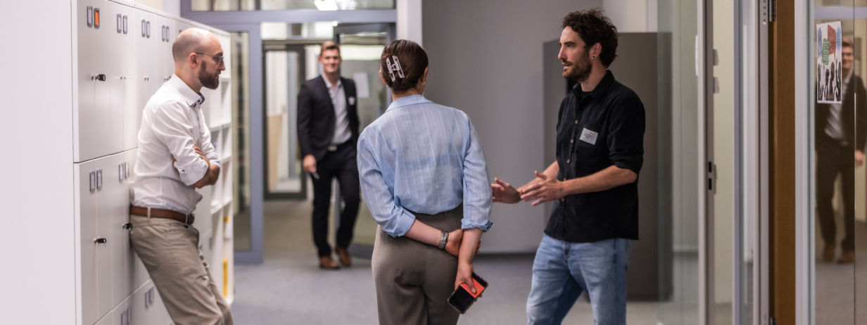 Drei junge Kolleginnen und Kollegen stehen redend auf Bürofläche zusammen.