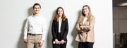 Drei selbstbewusste junge Menschen im Business-Look stehen vor weißem Hintergrund