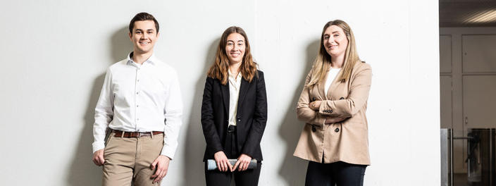 Drei selbstbewusste junge Menschen im Business-Look stehen vor weißem Hintergrund