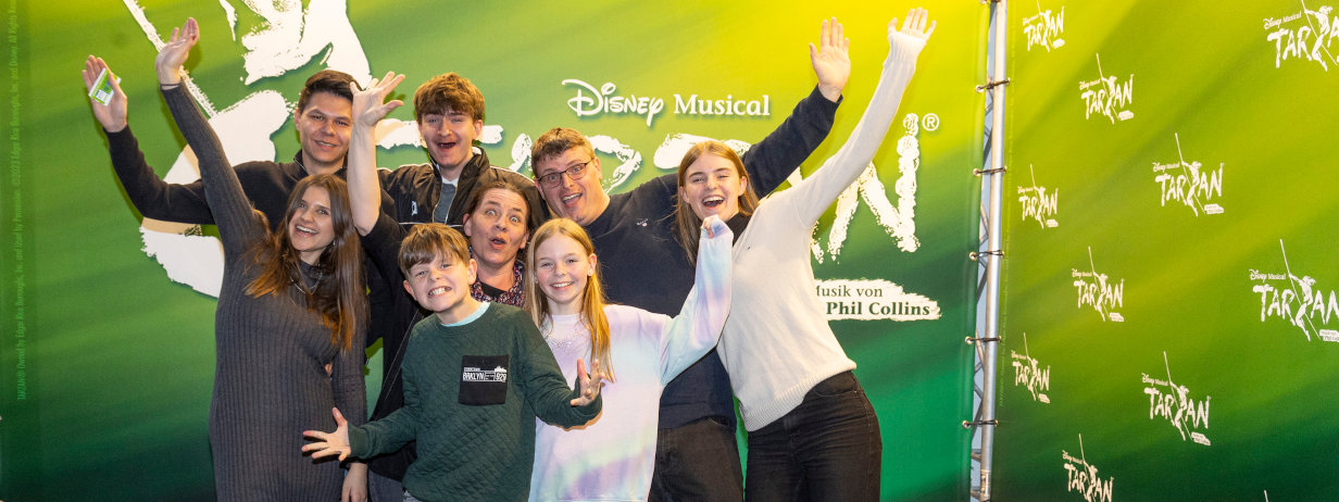 Gut gelaunte Familie mit Kindern vor grüner Wand beim Disney-Musical Tarzan