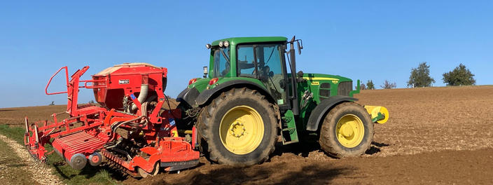 Traktor mit Sämaschine fährt bei blauem Himmel über ein gepflügtes Feld