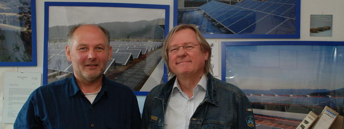 Dr. Josef Petsch (links) und Gilbert Kümmerle vor der Bürowand mit Fotos von Solarprojekten der Energiegenossenschaft fesa Energie Geno eG.