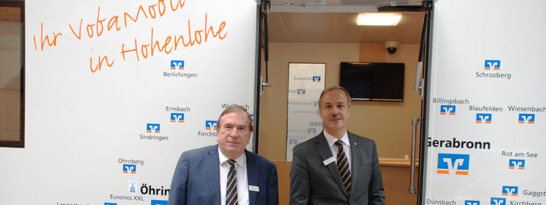 Edmund Wahl, Vorstandsvorsitzender der Volksbank Hohenlohe eG (links zu sehen) und Vorstandsmitglied Dieter Karle vor dem VobaMobil.